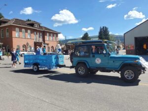 A teal-colored jeep pullling a parade float that looks like a pool with a stuffed animal bear on the diving board.
