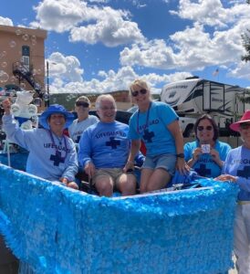 A group of smiling people sitting in and standing next to the Pb Swims pool float in on Harrison Ave in the 2023 Boom Days parade